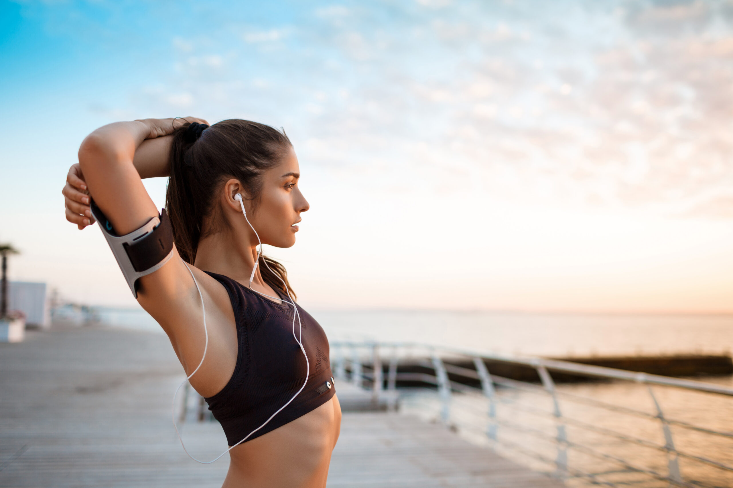 Young beautiful brunette sportive girl training at sunrise over seaside. Copy space.